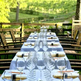 A table setting with several wine glasses and numerous place settings on tables with white table cloths and chairs.