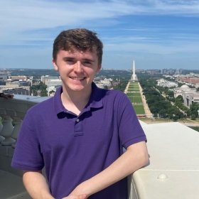 Spencer Rada stands on a balcony overlooking the National Mall with a view of the Washington Monument.