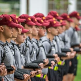 A group of Rooks stand in a line, all wearing grey shirts, maroon Rook hats, and holding shirts.