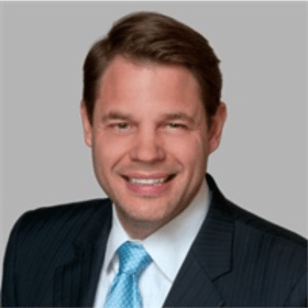 A formal headshot of Paul Fousek in a suit.