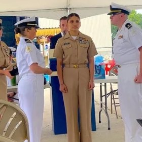 U.S. Navy officers in uniform participating in a formal ceremony under a tent.