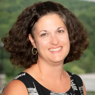 Person with curly dark hair wearing a black sleeveless top with white abstract patterns.