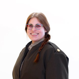 Person with glasses and a braid wears a dark coat and faces the camera.