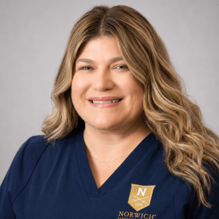 Person with curly hair wears navy Norwich University School of Nursing scrubs.
