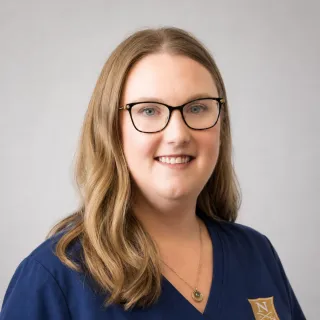 Person wearing glasses and navy Norwich University School of Nursing scrubs.