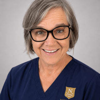 Person with short gray hair and glasses wears navy Norwich University School of Nursing scrubs.