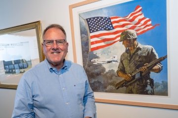 Person smiling and standing in front of a painting depicting a soldier with the American flag in the background.