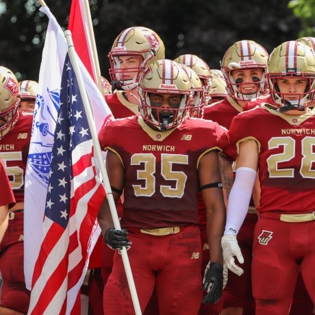 Jehric hackney stands in the center of his team while holding an American flag and preparing to run onto the football field.