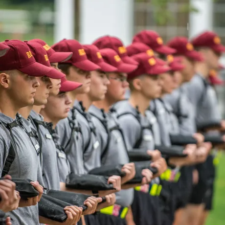 A group of Rooks stand in a line, all wearing grey shirts, maroon Rook hats, and holding shirts.