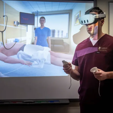 Person in medical scrubs using virtual reality equipment, interacting with a simulation displayed on a screen showing a hospital room scenario.