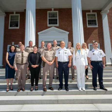 Group of uniformed military personnel and civilians posing together on steps in front of a building with large columns.