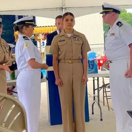 U.S. Navy officers in uniform participating in a formal ceremony under a tent.