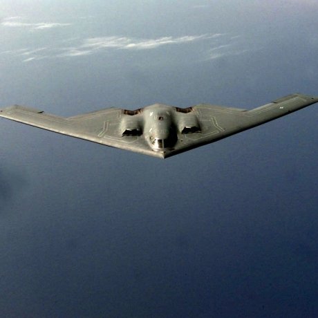An overhead photo of a B-2 bomber flying over water.