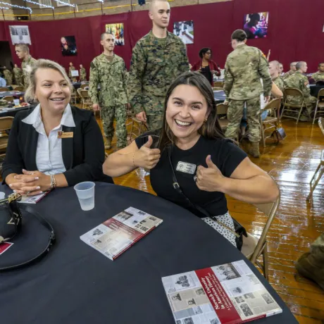 A Norwich student grins and gives two thumbs up during the First Contact event as a group of cadets walks behind her.
