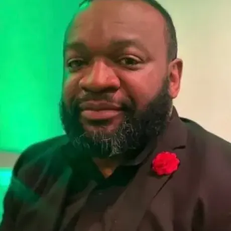 raheem Berry in a black shirt and suit portrait style.