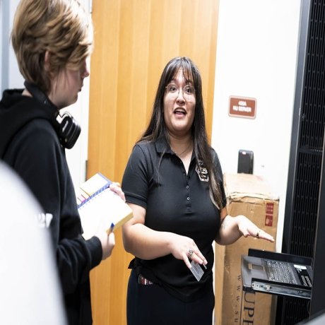 A woman stands in front of a computer server, instructing an observer.