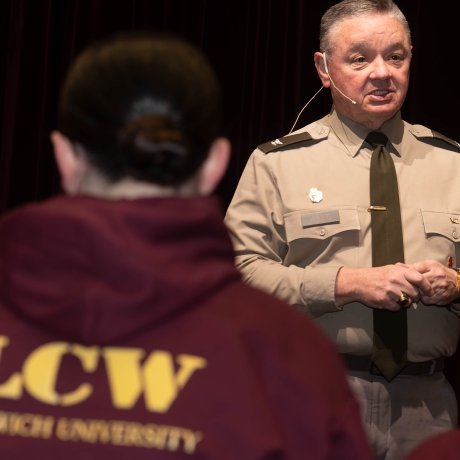 Person in uniform speaks to people wearing maroon hoodies labeled LCW Norwich University.