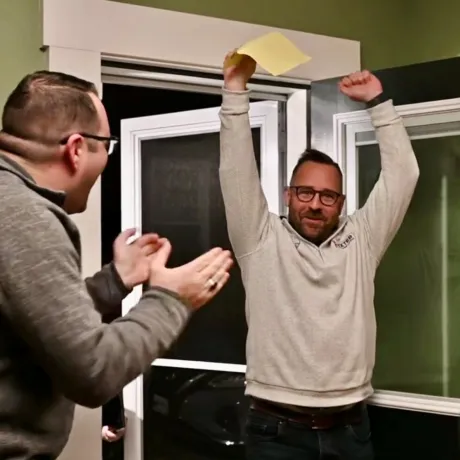 a man in foreground, facing another man with hands in air, holding a paper ballot