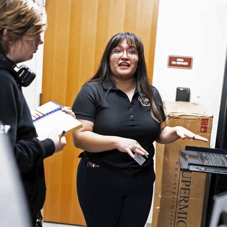 A woman stands in front of a computer server, instructing an observer