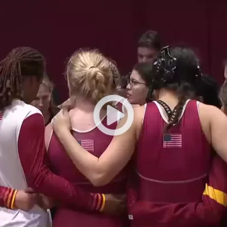 Group of athletes in maroon and gold uniforms with USA flags on their backs huddling together in a gymnasium.