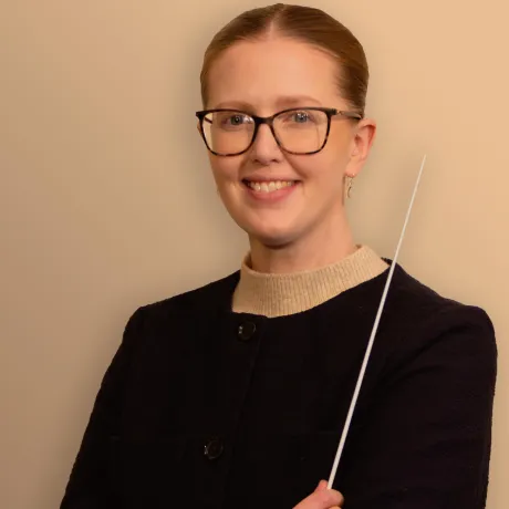 Person in a dark jacket holds a thin baton against a plain background.