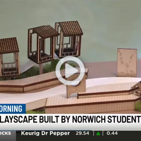 Model of a wooden playscape with small structures and ramps shown in a news graphic labeled “Library Playscape Built by Norwich Students.”