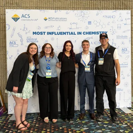 Five people pose with conference badges in front of an ACS Chemistry for Life backdrop.