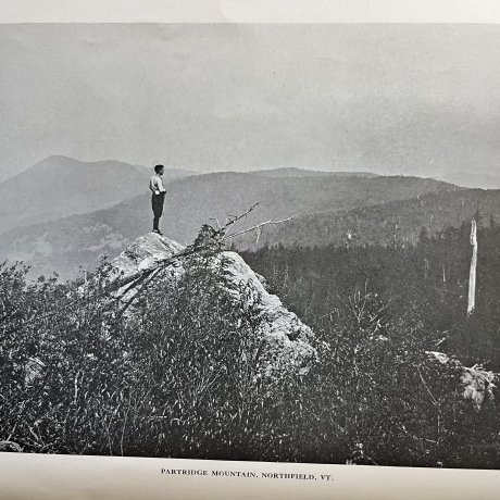 A person stands on a rocky ledge above Partridge Mountain in Northfield, Vermont.