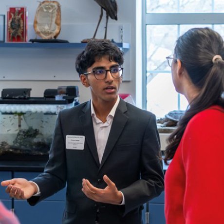 Student in a suit speaks with another person in a classroom.