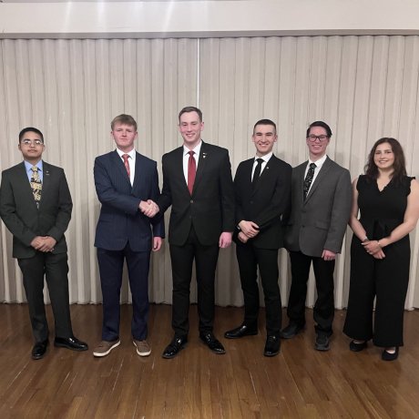 people in formal attire stand in a line as two men in the center shake hands.