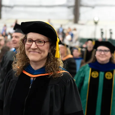 Person in academic regalia and tam walks in a graduation procession.