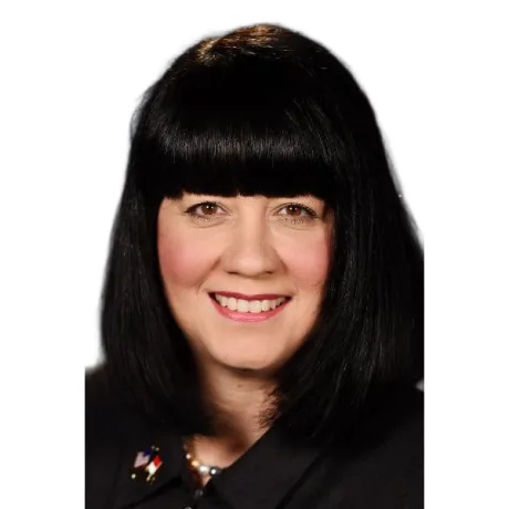 Headshot of a person with black hair and bangs smiling against a light gray background.