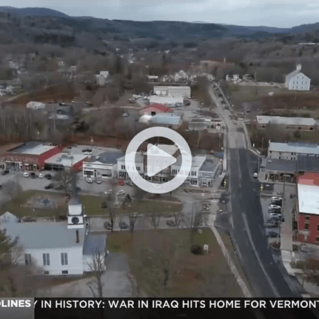 Aerial view of a small town with roads, buildings, and hills in the background.