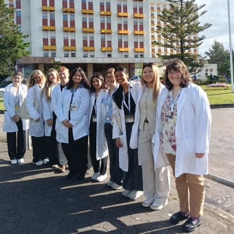 Group of students in white lab coats stand outside Coimbra University Hospitals building.