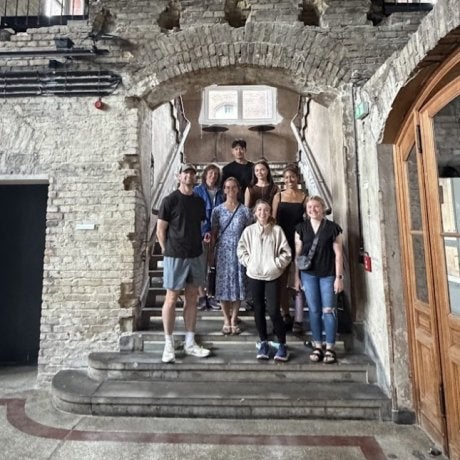 Eight people stand on stone steps beneath a brick archway inside a historic building.