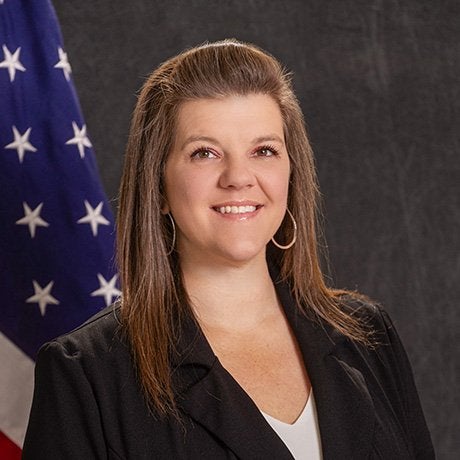 Vanessa Middleton profile image in a black blazer and white top standing in front of a U.S. flag and dark backdrop.