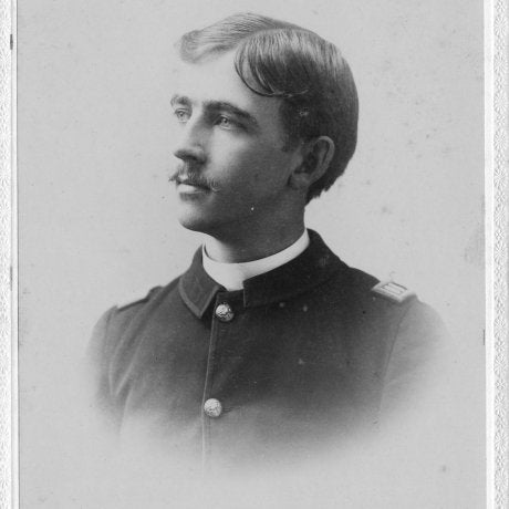 Service member in a dark uniform poses in profile for a studio portrait.