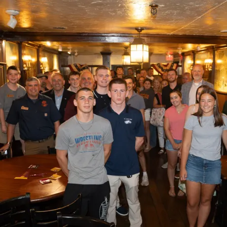 A large group poses together inside a wood-paneled room.