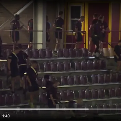 Students in matching shirts walk through stadium seating and gather near a doorway.