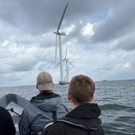 Two people ride in a boat toward offshore wind turbines.