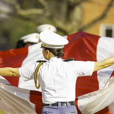 A cadet in a white uniform holds out a large red and white fabric banner