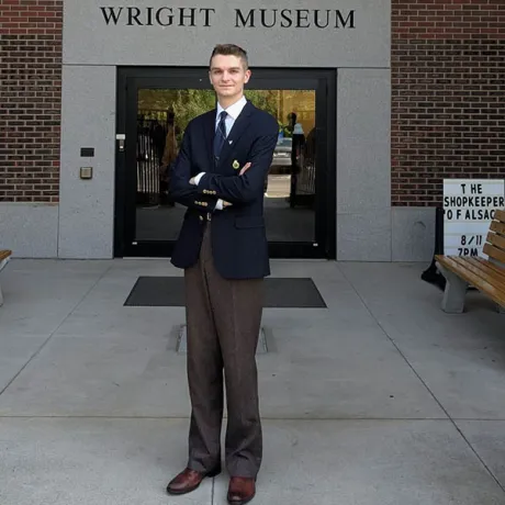 A person in a blazer stands with arms crossed outside the Wright Museum entrance.