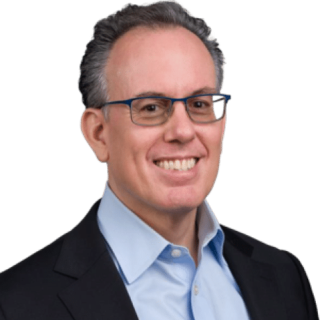 Portrait of a person wearing glasses, a dark blazer, and a light blue collared shirt.