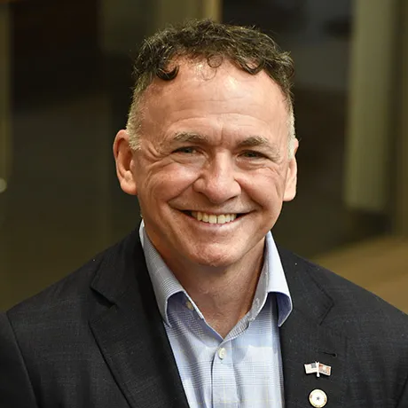 Sean O’Brien ’90: Sean O’Brien smiles for a headshot, wearing a dark blazer over a light blue collared shirt.