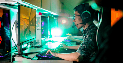 Esports gamer playing on a computer with glowing keyboard and high-tech equipment surrounding him.