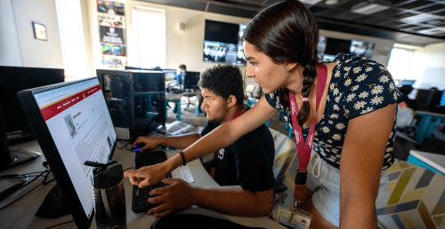 Two students working together on computers. Girl points to computer screen.