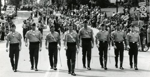 six Norwich cadets marching in formation, in foreground, in a parade