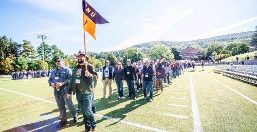 man in cowboy hat holding flag, and man in baseball cap, lead a long line of other Norwich alumni in the Norwich homecoming alumni parade in 2021.