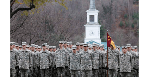a large number of Norwich Cadets in review formation stand with a chapel steeple in the background.