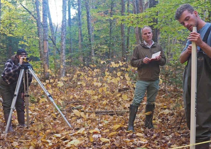 Two students working with faculty to take measurements in the woods.